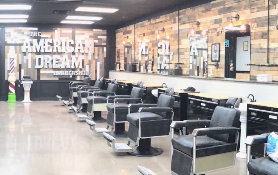 Row of black leather barber chairs in front of mirrors and a reclaimed-wood wall